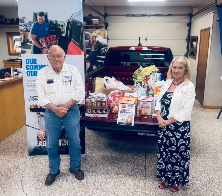 Man and woman pose with a pickup truck bed full of food donations.